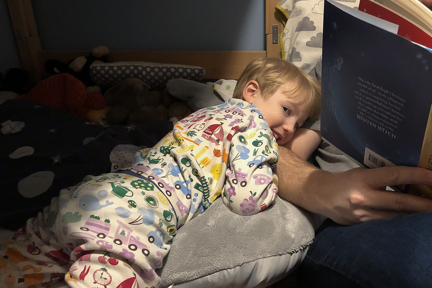 A small boy cuddling up to a man's arm which is holding a book