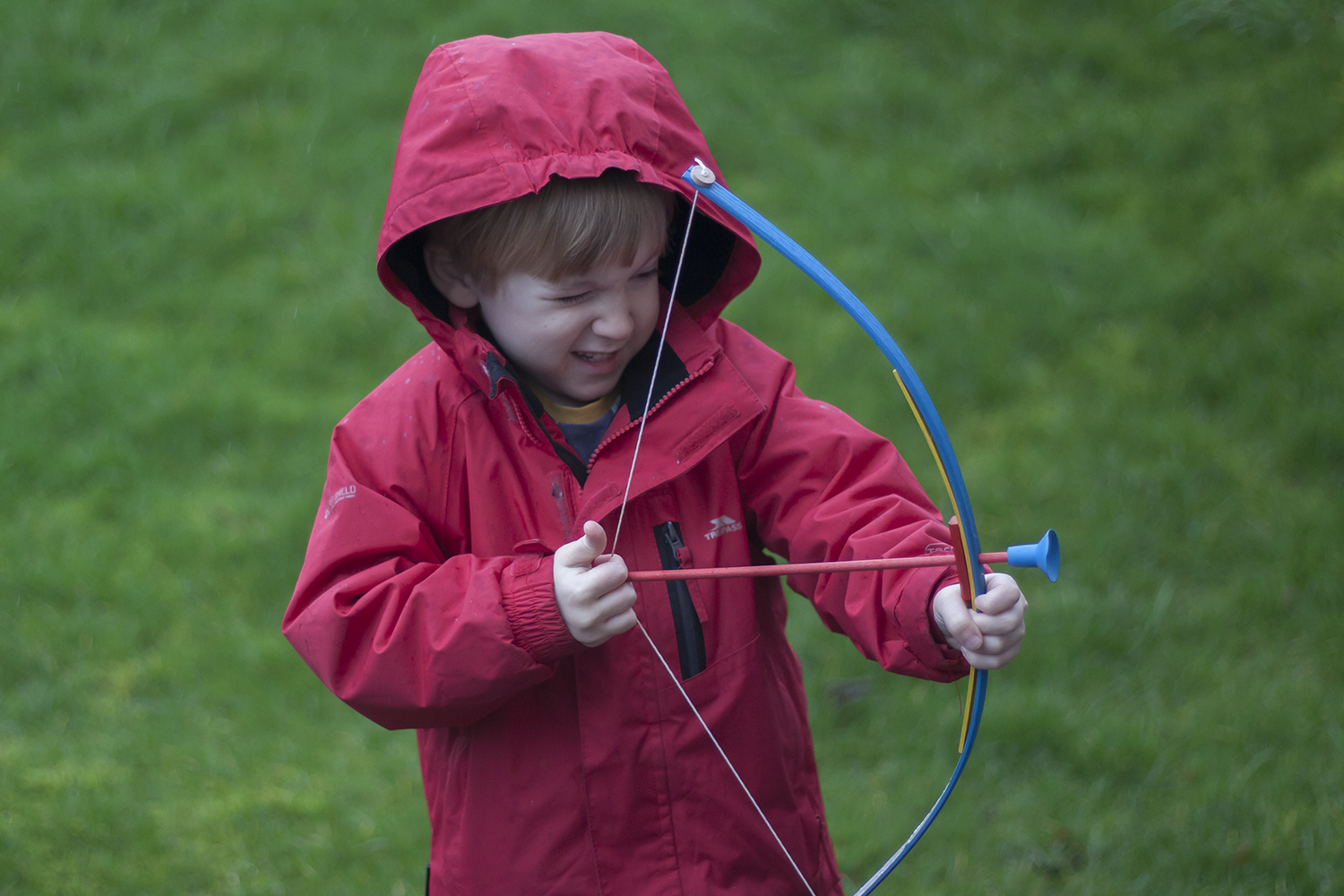 A boy in a red coat with a wooden bow and arrow