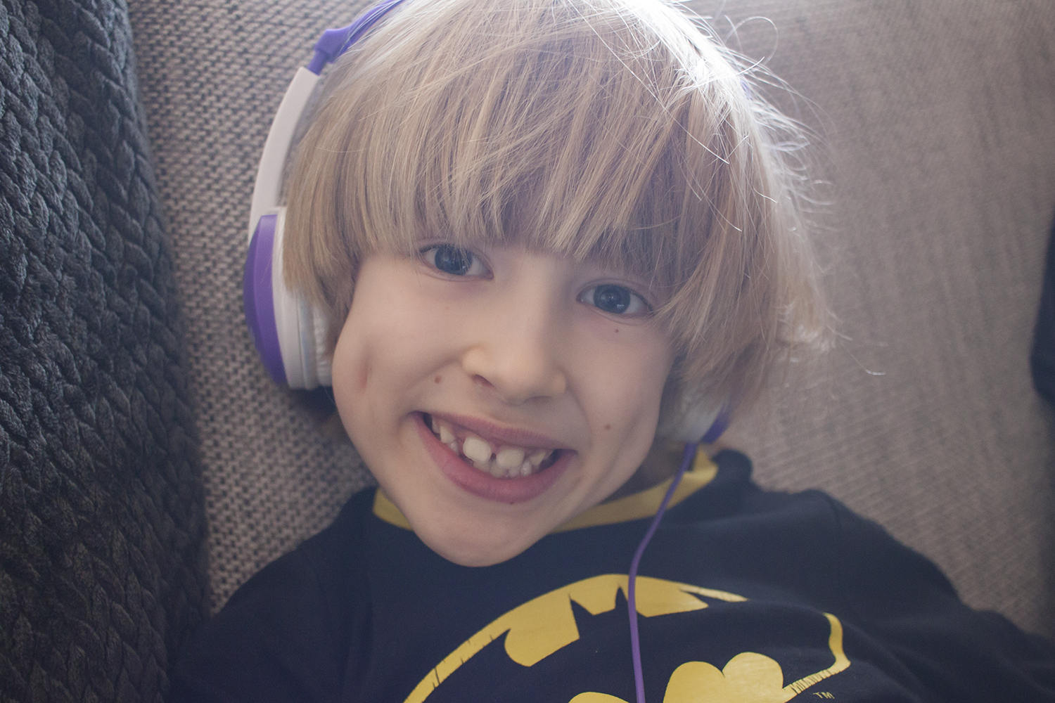 A boy with a batman t-shirt wearing purple and white headphones