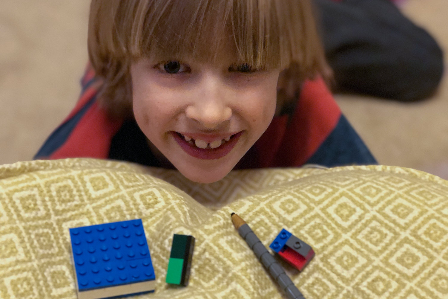 A boy grinning with some Lego on a cushion in front of him