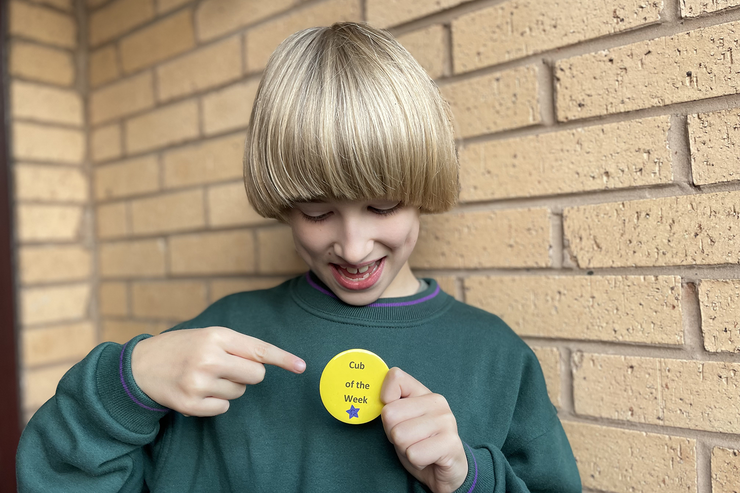 Toby in a green Cub jumper holding a yellow 'Cub of the Week badge