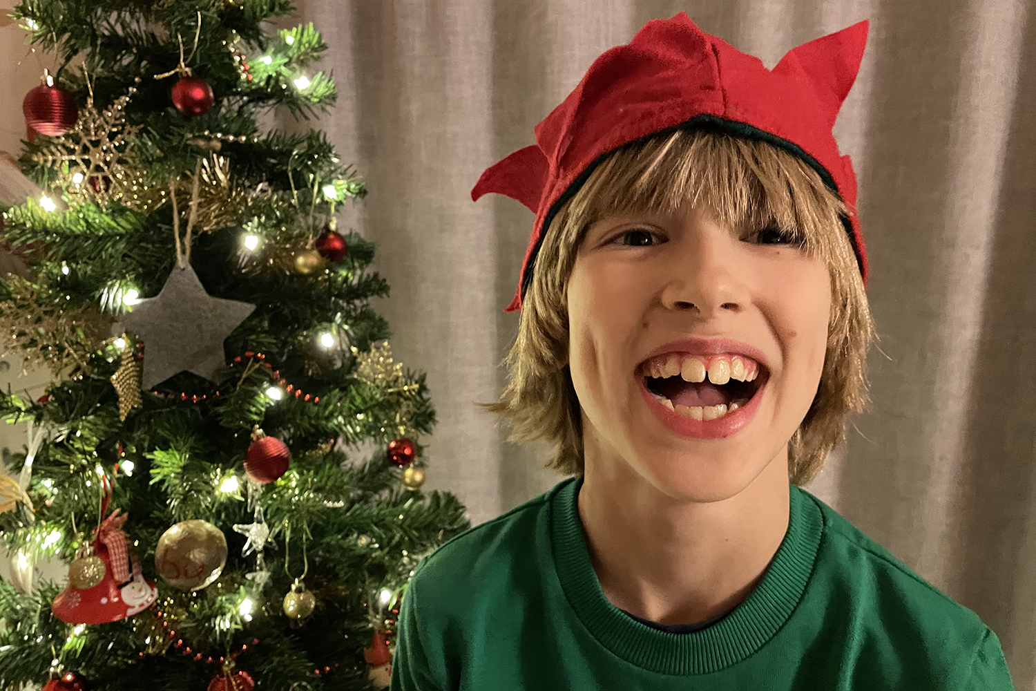Toby wearing an elf hat and laughing in front of the Christmas tree