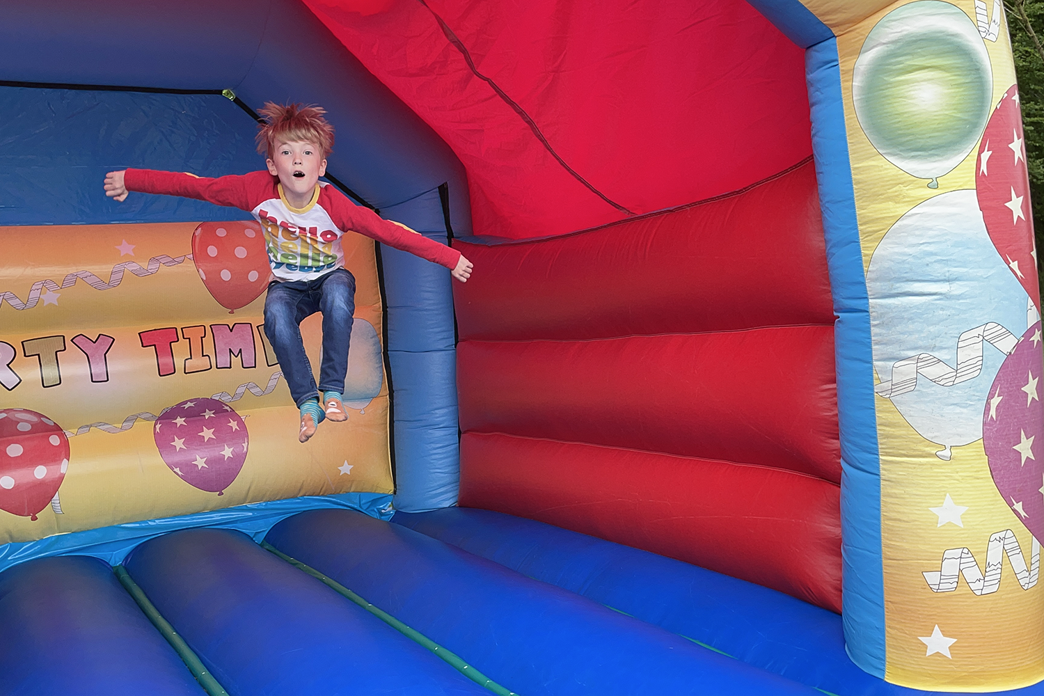 Gabe doing a massive jump on a blue and red bouncy castle.